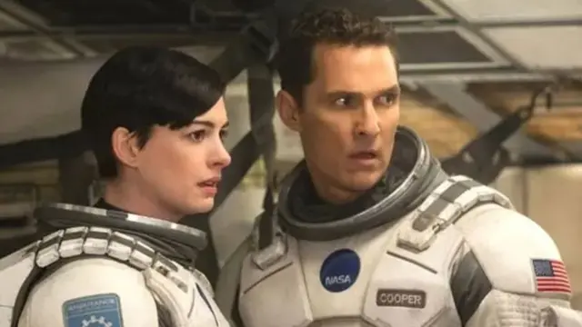 Matthew McConaughey e Anne Hathaway com roupas de astronauta e olhar de espanto, observando algo; os dois estão próximos e em pé
