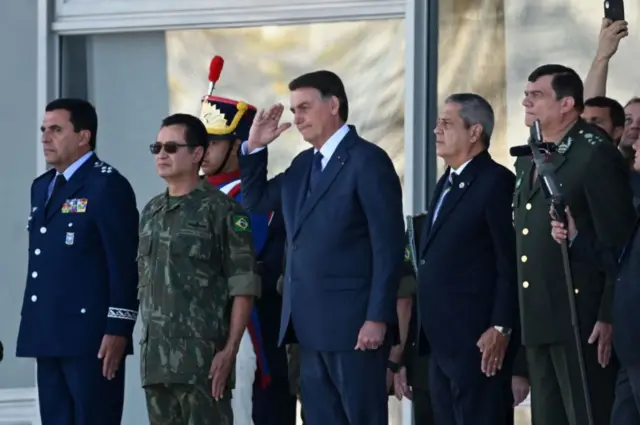 Bolsonaro faz continência durante evento. Ao lado dele há vários militares